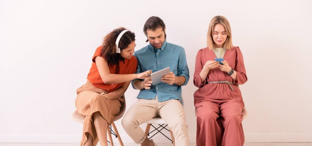 three people, woman listening to music with headphone on the left side, a man watch his ipad in the middle, and a short hair girl whats her phone on the right side