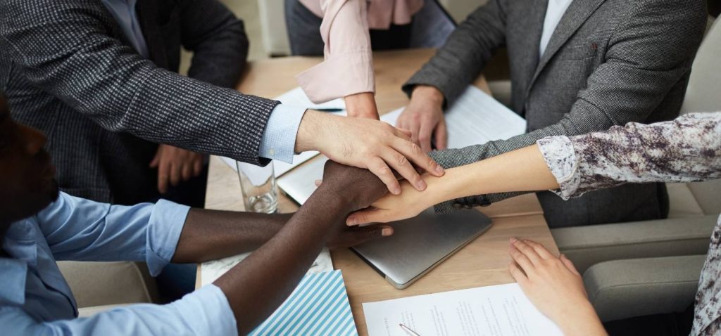 5 fists of a marketing team come together in the middle to show symbolic strength and in utilizing marketing tools.
