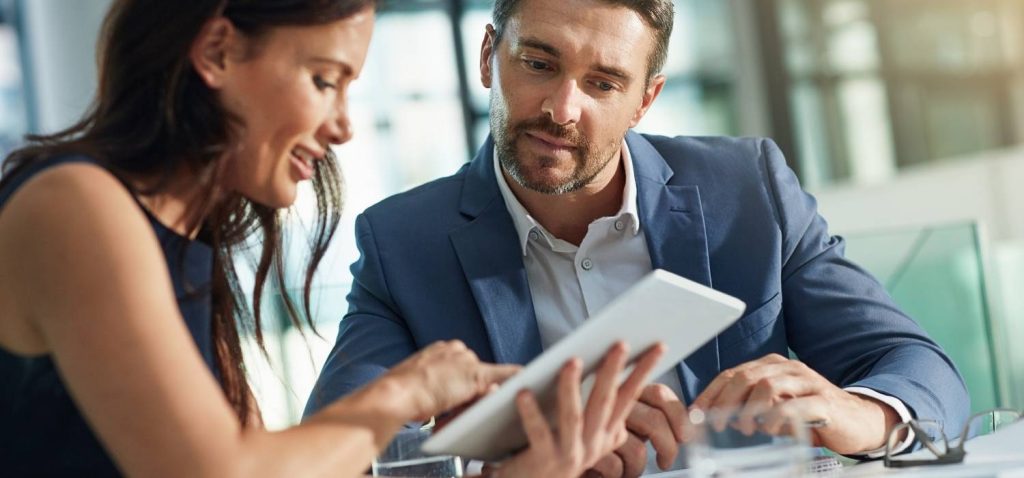 two people, one pretty woman and one handsome man sit together in the office discussing about technology business in their ipad