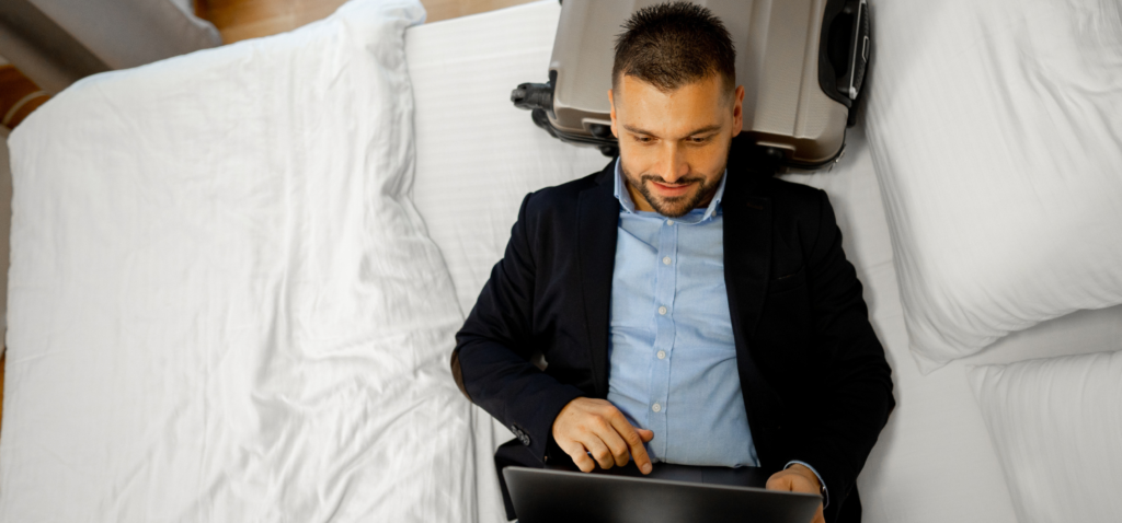 Male businessman taking a rest on his hotel bed while playing with his laptop on his business trip