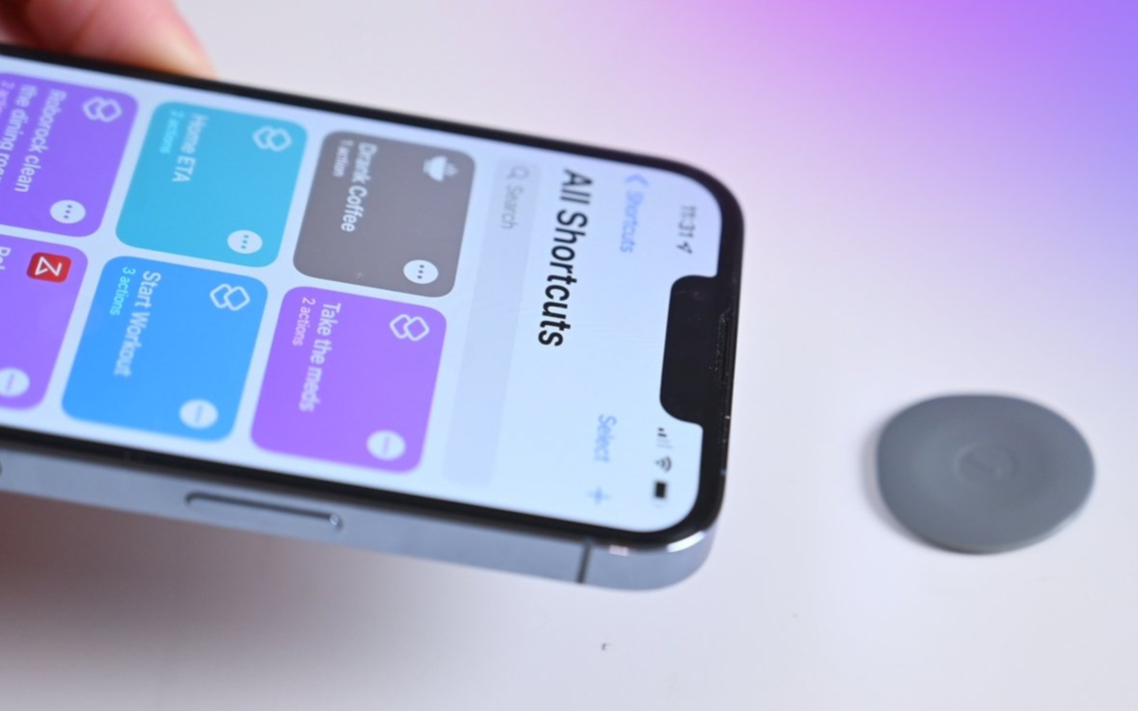 A person's finger holding an iPhone 14 to bring it closer to the NFC Smart Tag GOTAP on a white table with a purple gradient as the background