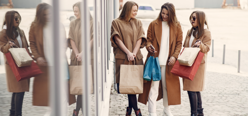 tiga wanita mengenakan mantel musim dingin berwarna cokelat membawa tas belanja sebagai contoh perilaku pelanggan untuk kampanye pemasaran nfc