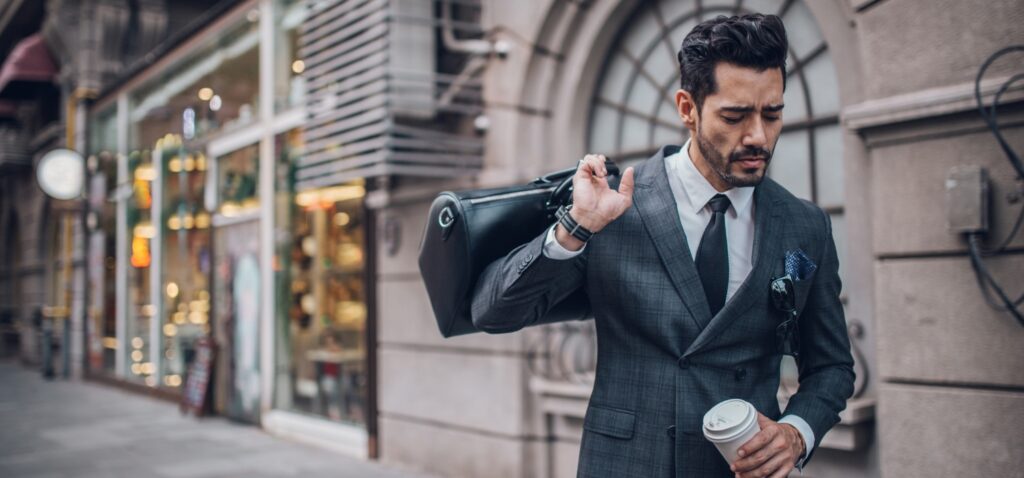 Seorang manajer yang menggunakan kartu pintar GOTAP dengan setelan jas hitam yang rapi membawa koper hitam yang berisi anggaran perjalanan bisnis dan gelas berisi kopi panas.
